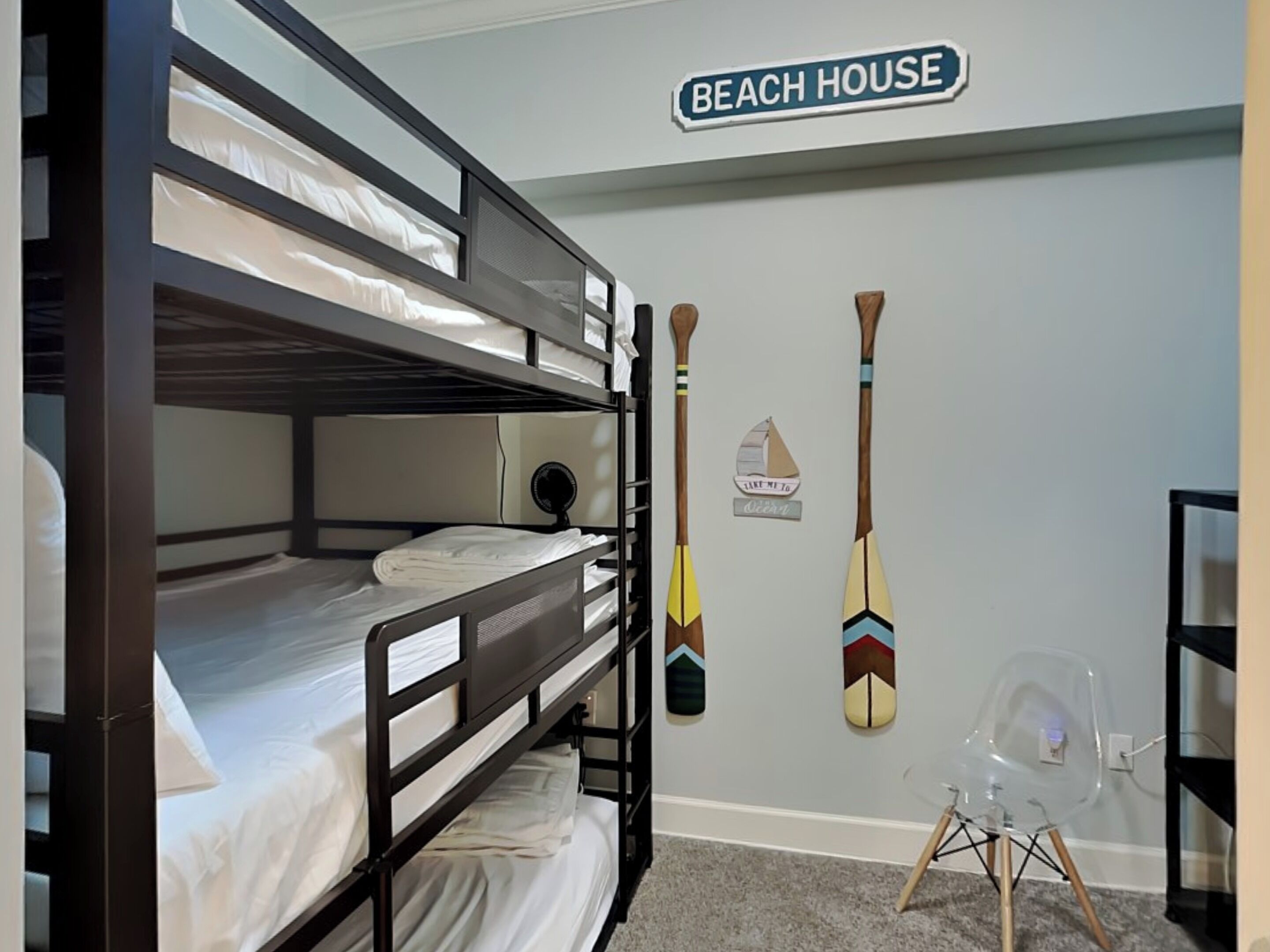 Habitación con literas, un cartel que dice 'BEACH HOUSE' y dos tablas de remo en la pared.