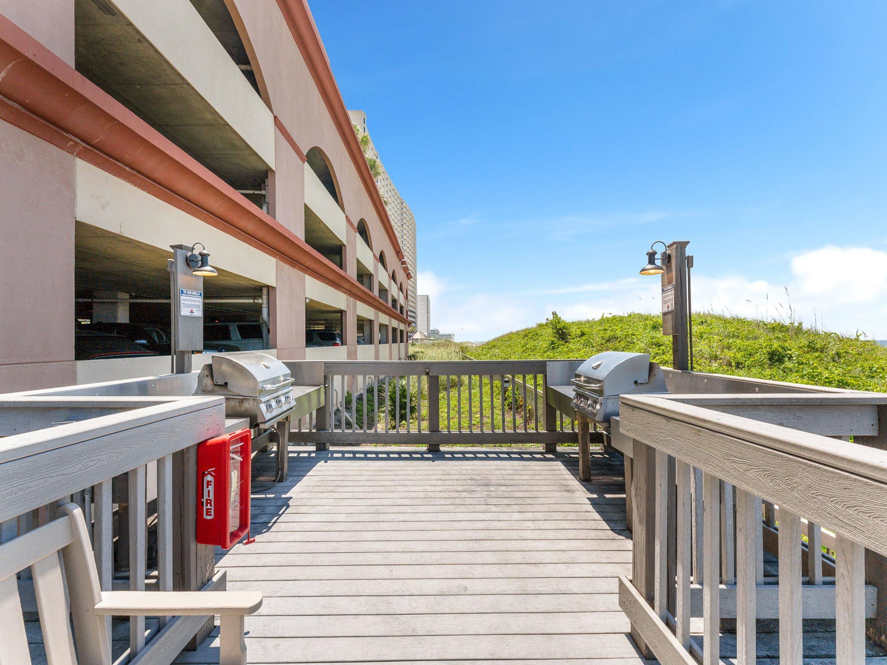 A wooden deck leading to a parking garage with a fire extinguisher and a barbecue grill.