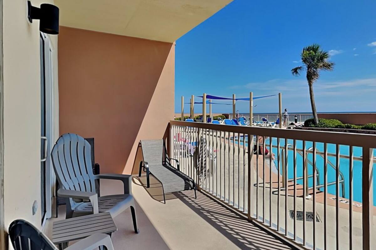 A balcony with a pool view, chairs, and a railing.