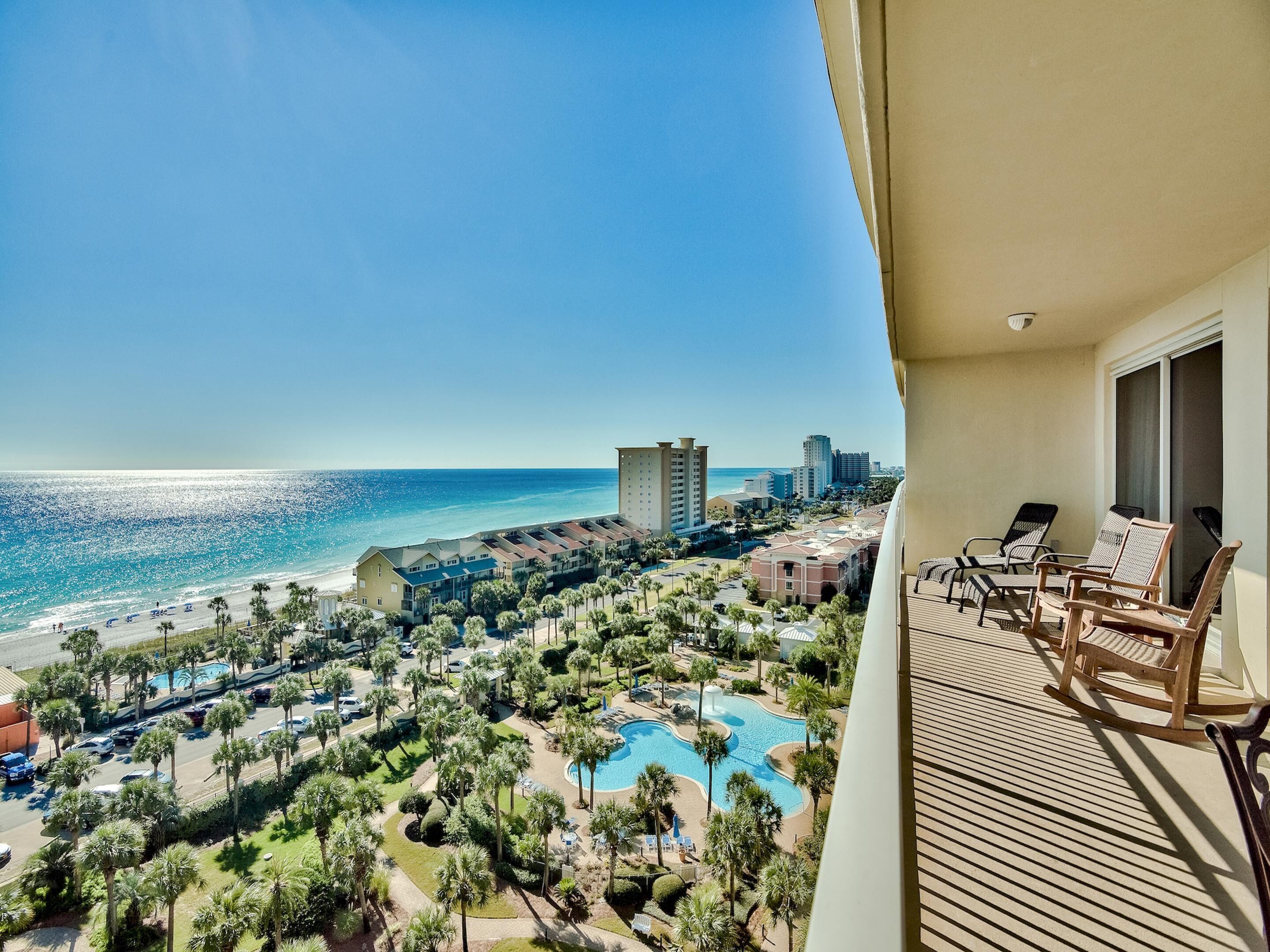 A balcony with a view of a beach, a pool, and surrounding buildings.