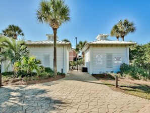 A pathway leading to two white buildings with palm trees and a sign indicating pool rules and no lifeguard present. - Sterling Shores by Southern Vacation Rentals (Destin)