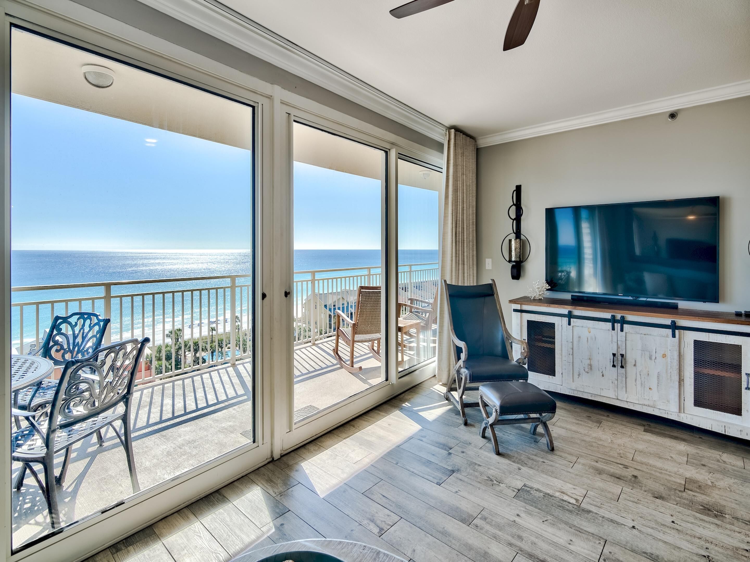A balcony with a view of the ocean, a TV, and a seating area with chairs and a table.