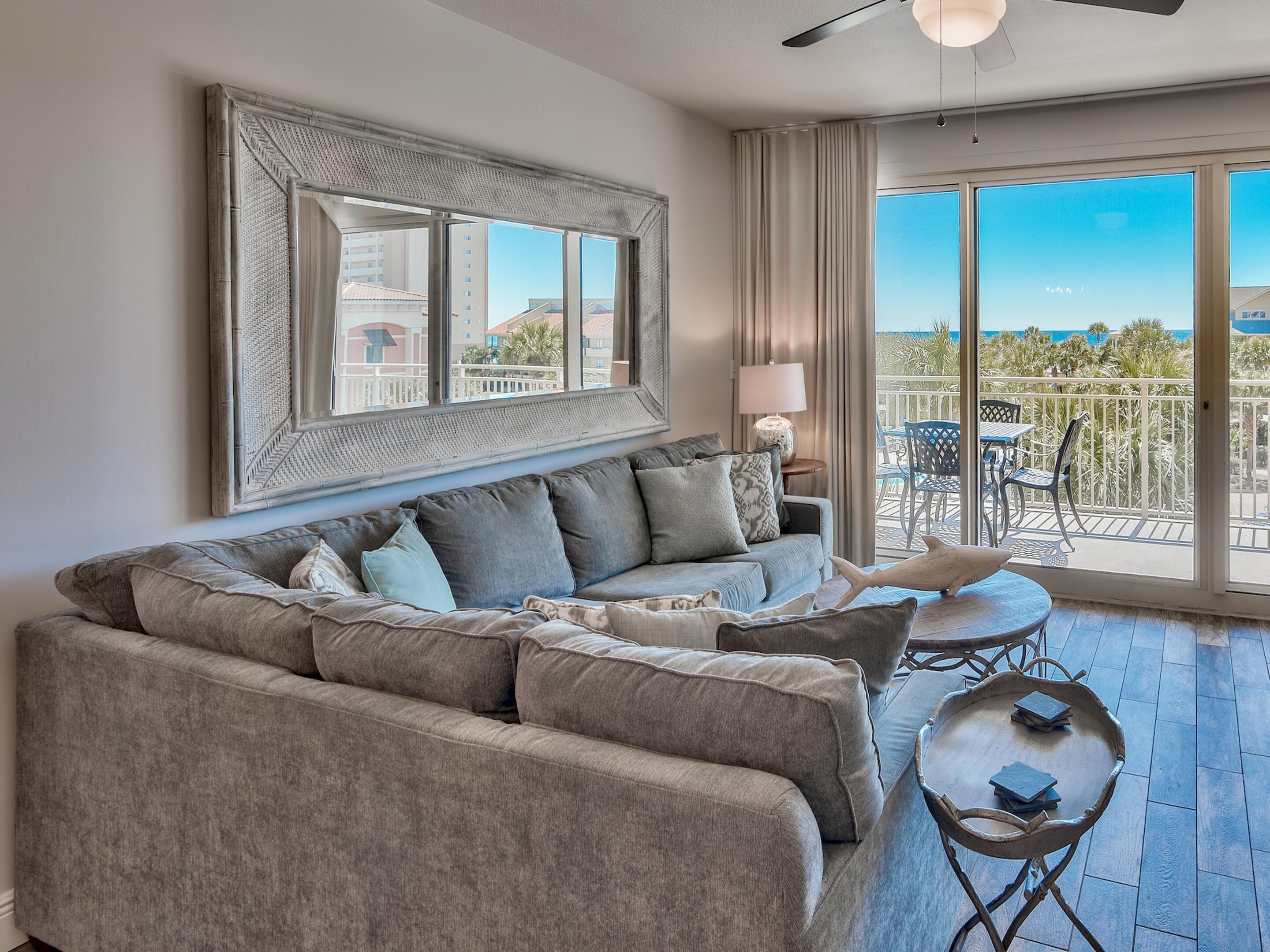 A modern living room with a large gray sectional sofa, a small round table with books, and a balcony with outdoor furniture.