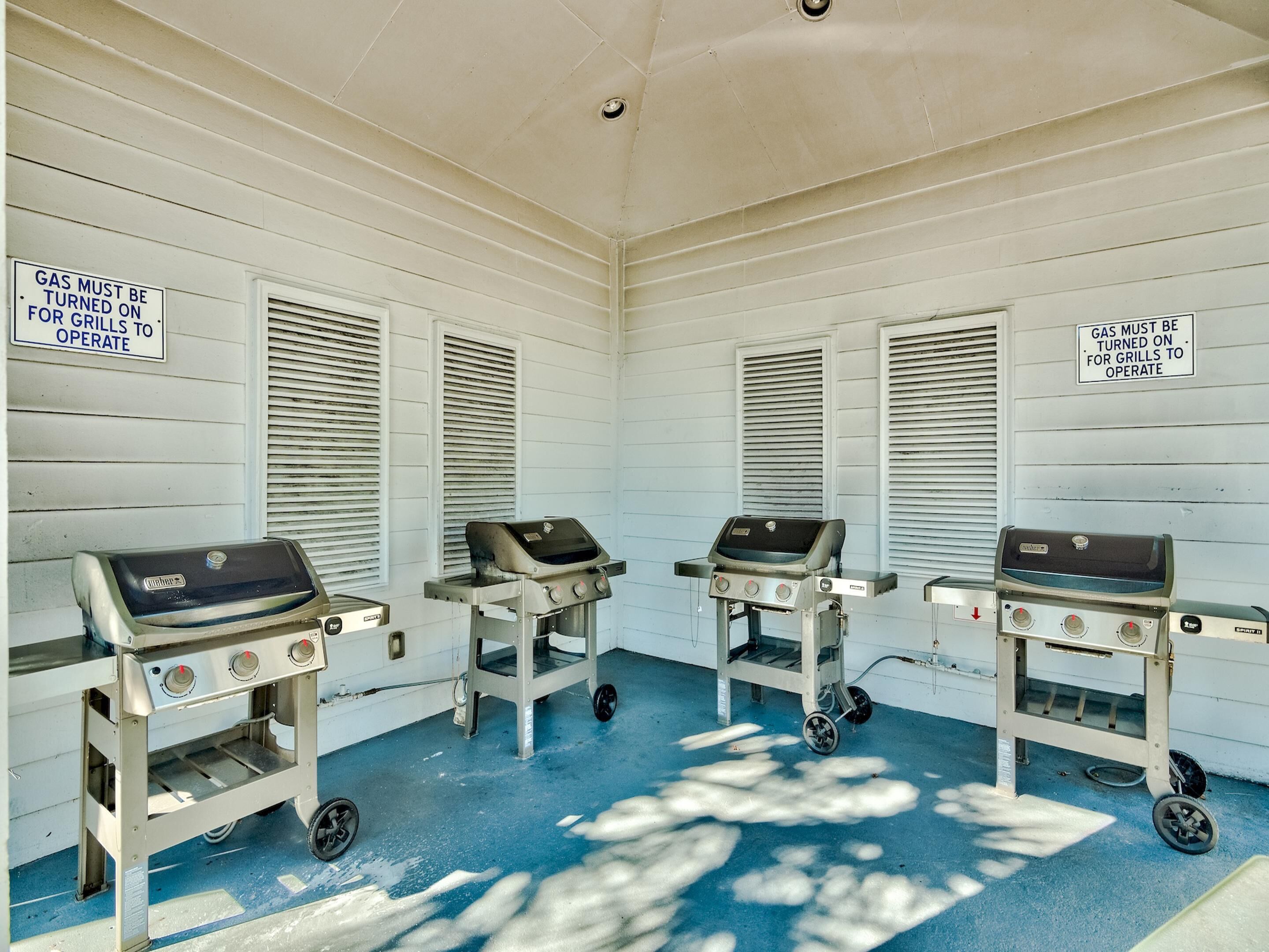 A room with three portable gas grills, each with a sign stating 'GAS MUST BE TURNED ON FOR GRILLS TO OPERATE'.