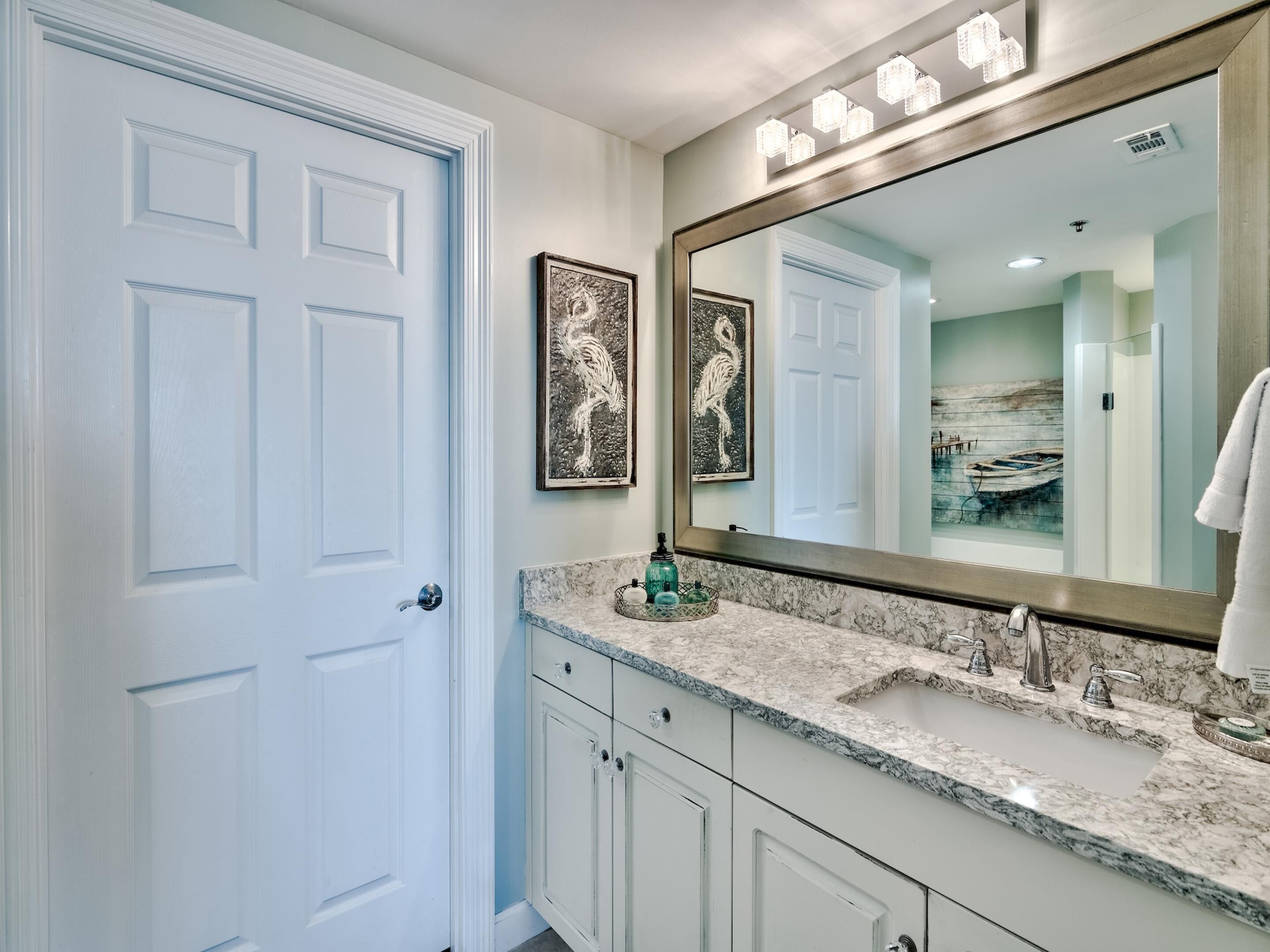 A bathroom with a white door, a large mirror, and a marble countertop.