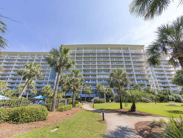 A multi-story hotel with a uniform exterior, surrounded by palm trees and a well-maintained lawn. - Sterling Shores by Southern Vacation Rentals (Destin)