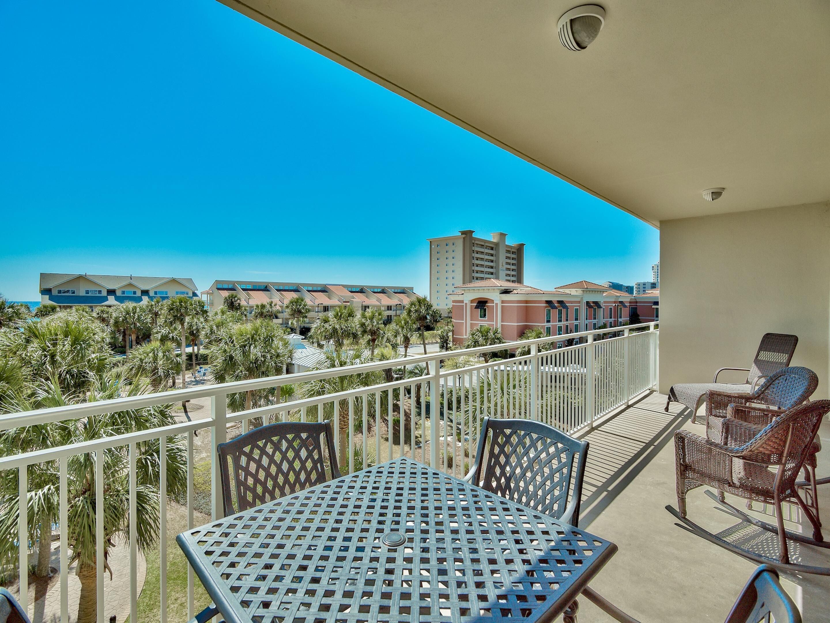 A balcony with a table and chairs, overlooking a view of buildings and palm trees.