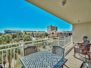 A balcony with a table and chairs, overlooking a view of buildings and palm trees. - Sterling Shores by Southern Vacation Rentals (Destin)