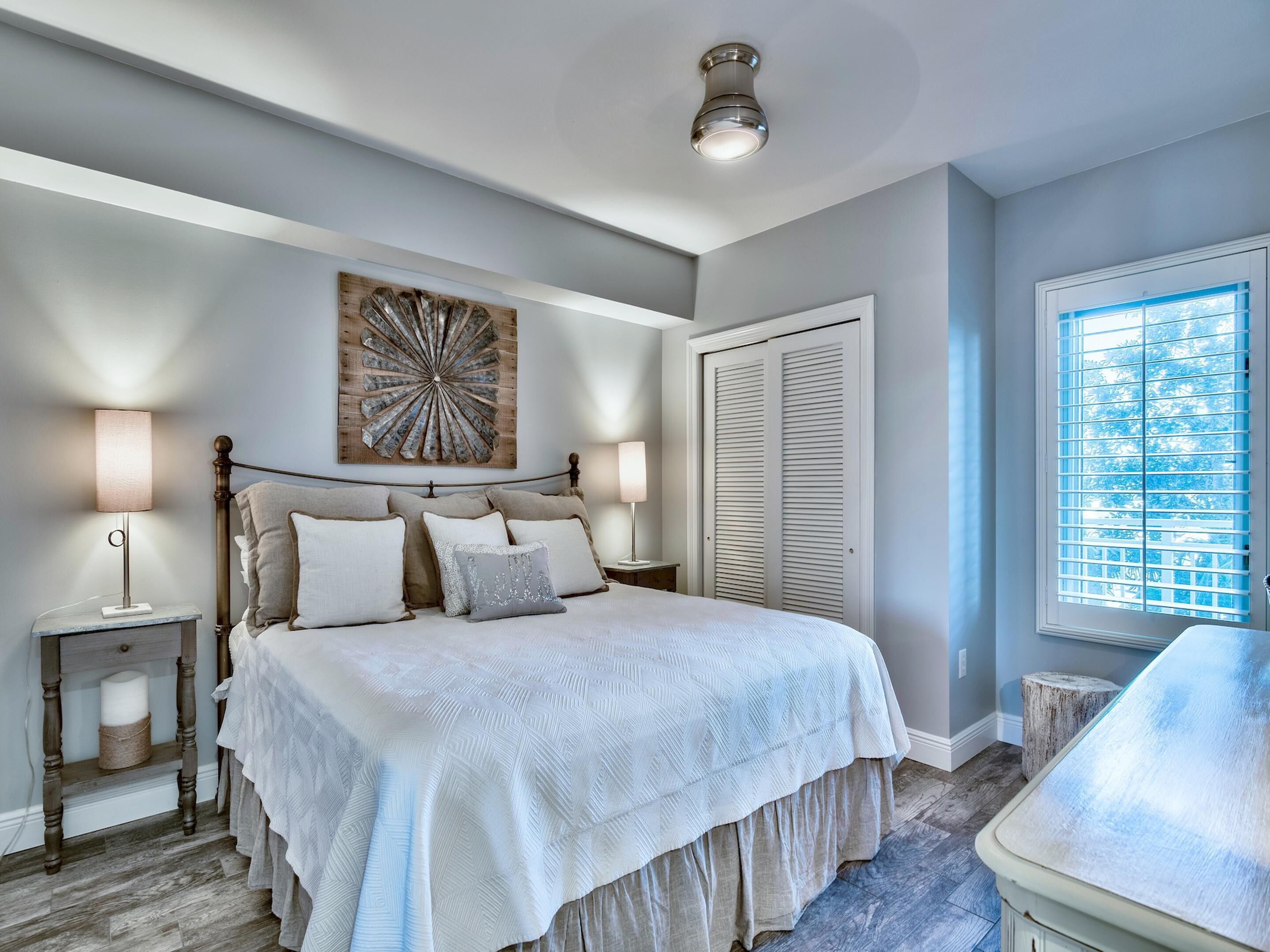 A bedroom with a bed, bedside lamps, a wall art piece, a closet, and a window with blinds.