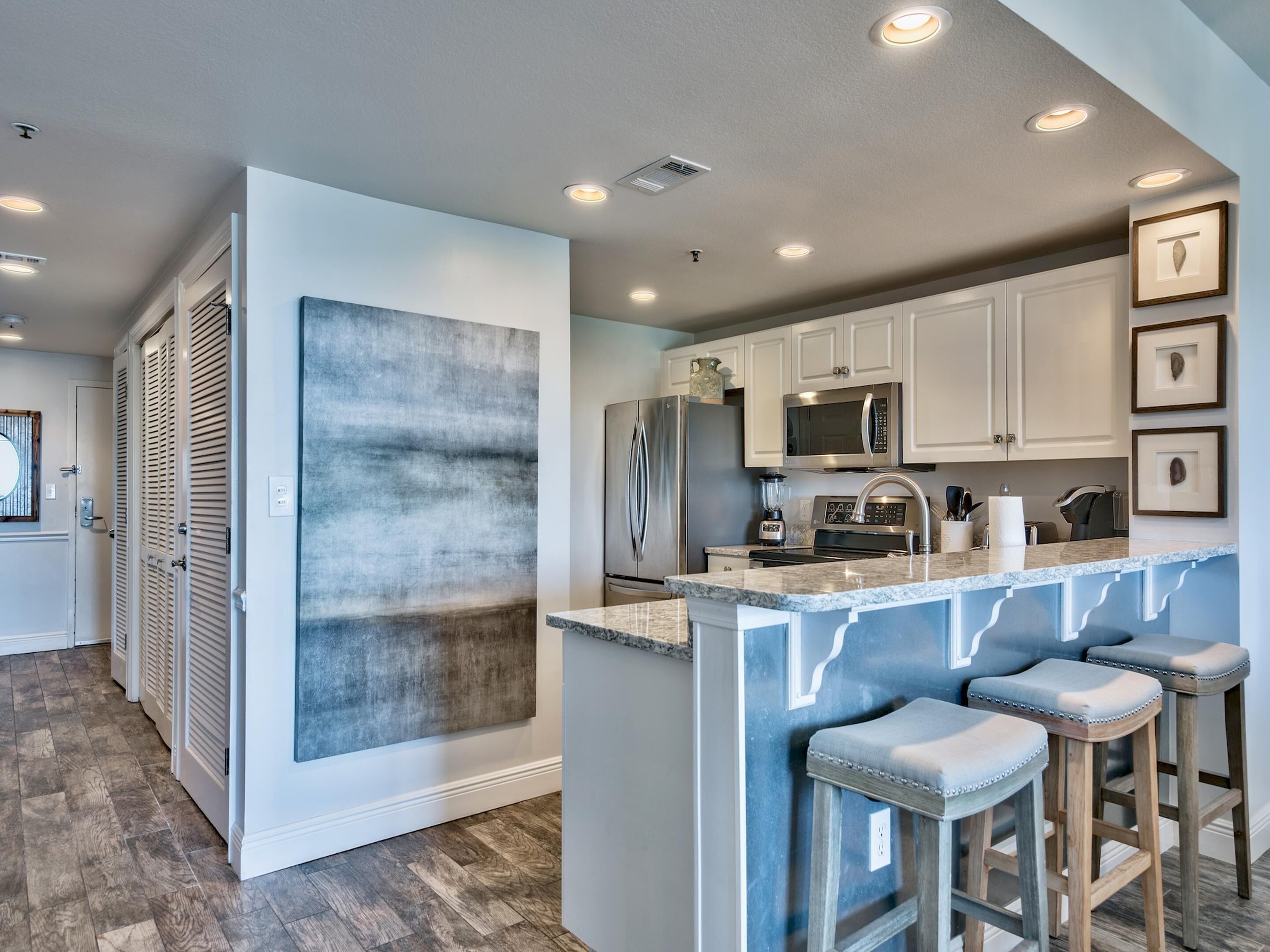 A modern kitchen with white cabinets, a stainless steel refrigerator, a microwave, and a built-in island with bar stools.