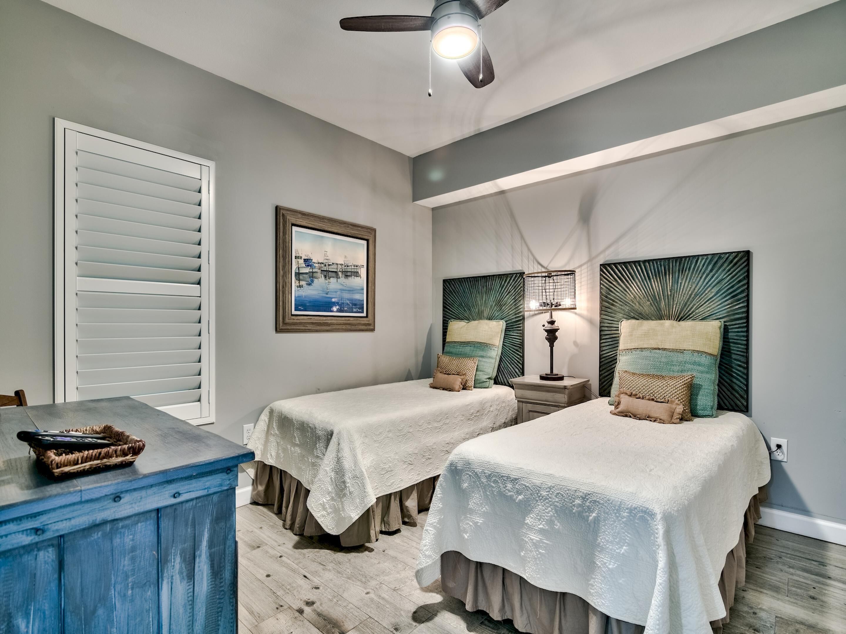 A bedroom with two beds, a ceiling fan, a framed picture, and a nightstand with a lamp.