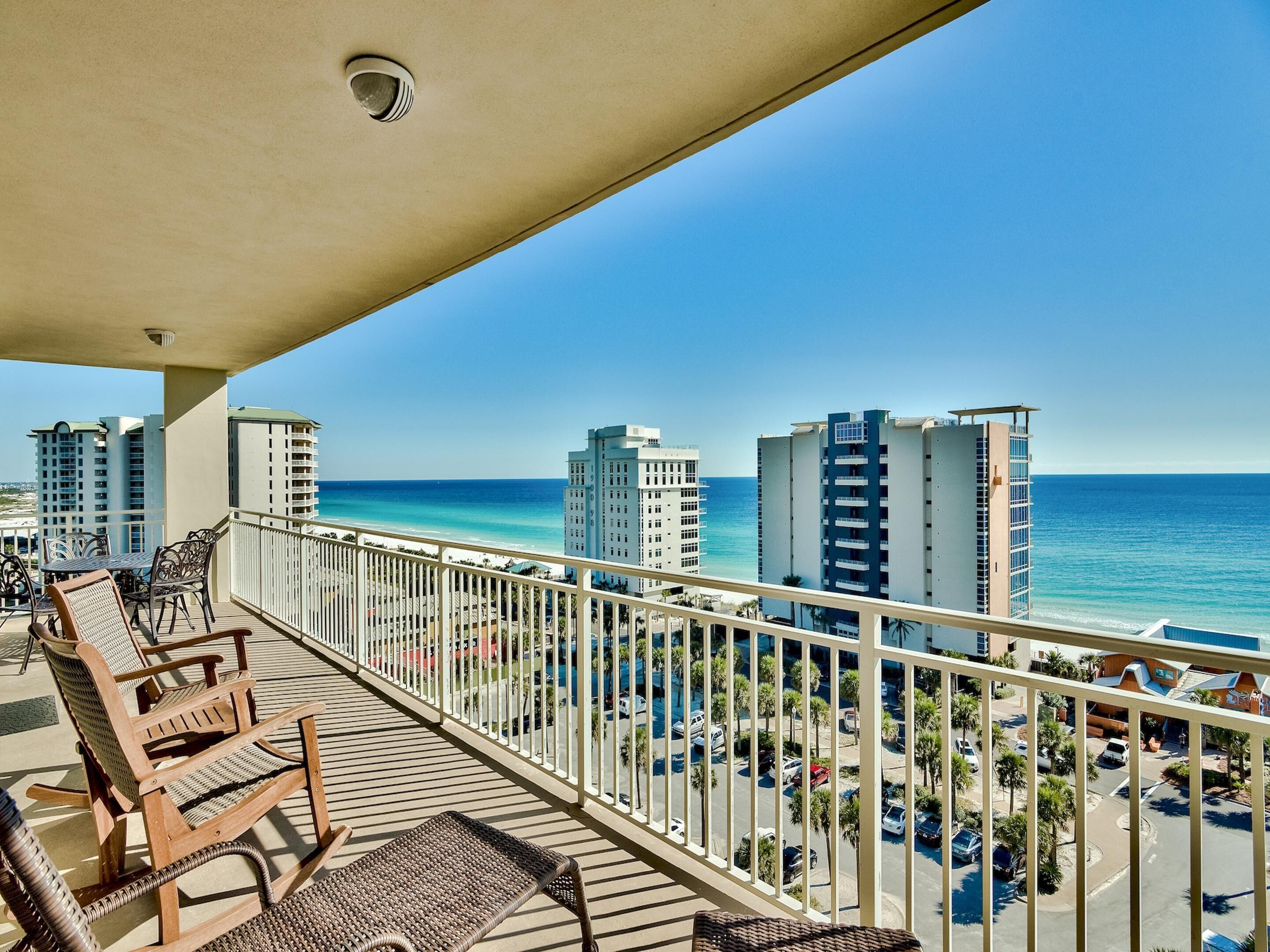 A balcony with wicker furniture overlooking a beach and cityscape.
