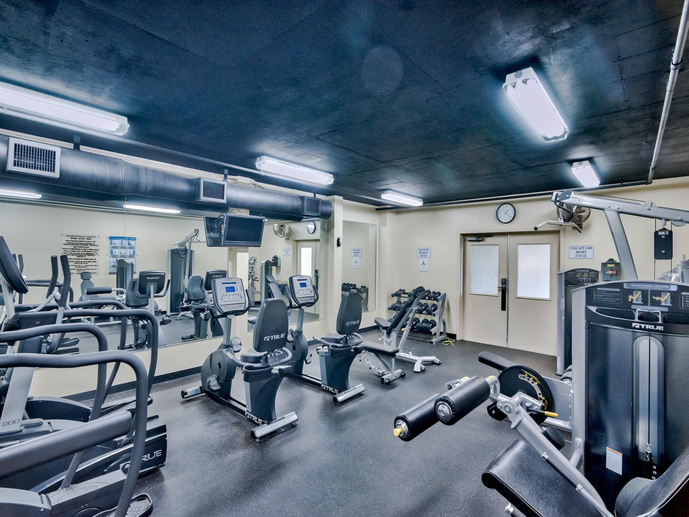 Ein Fitnessstudio mit verschiedenen Trainingsgeräten, darunter Laufbänder, Crosstrainer und Kraftgeräte.