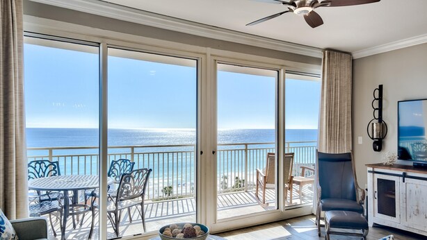 Un balcon avec vue sur l’océan, une table à manger avec un bol de biscuits et un coin salon avec un canapé et des fauteuils.