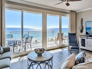A balcony with a view of the ocean, a dining table with a bowl of cookies, and a seating area with a sofa and chairs. - Sterling Shores by Southern Vacation Rentals (Destin)