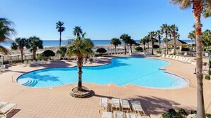 Zona de piscina amb disseny corbat, envoltada de palmeres i gandules, amb vista a una platja.