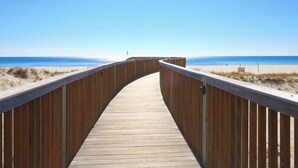 Una passera de fusta que condueix a una platja amb cel blau.