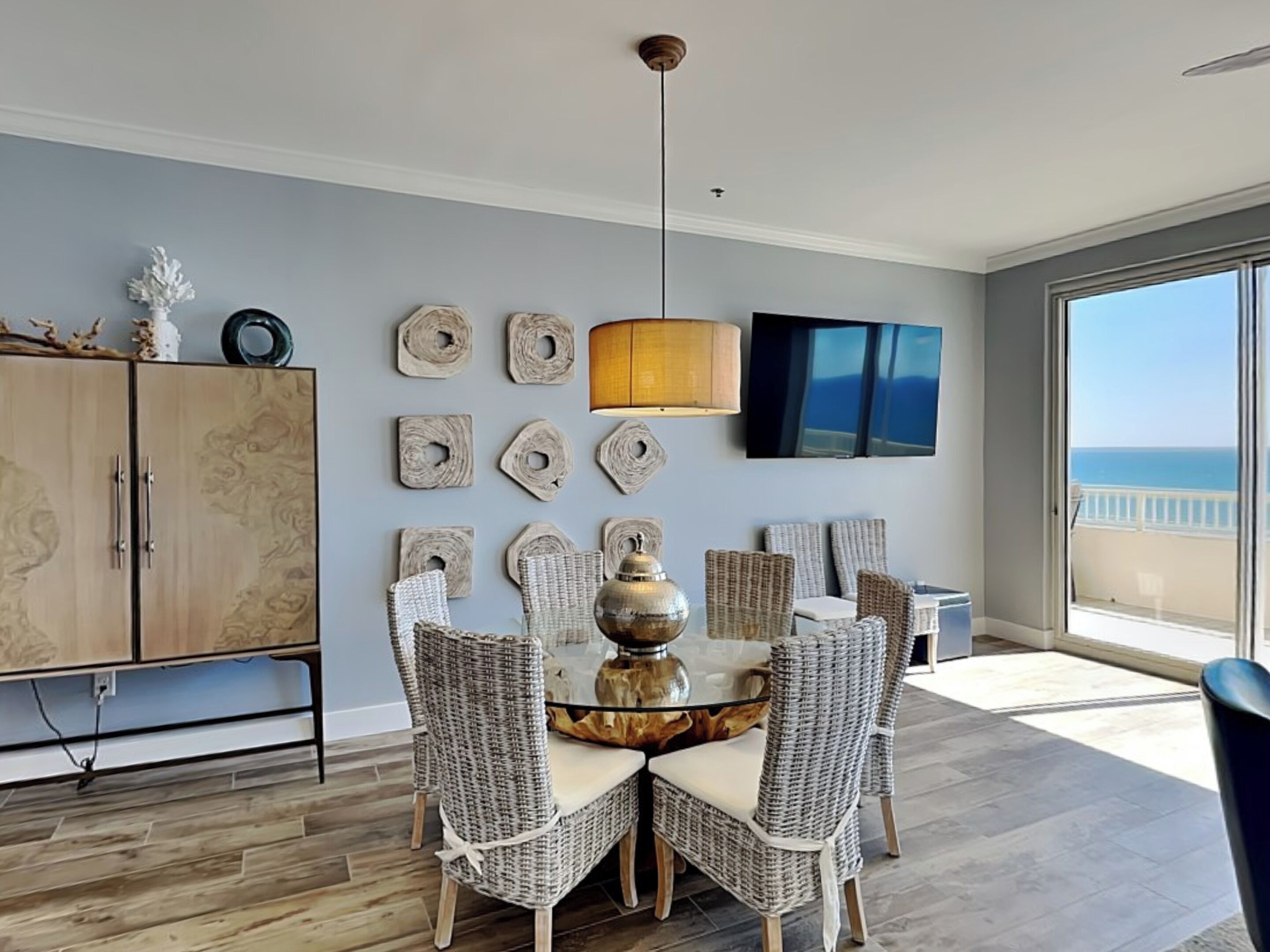 A dining area with wicker chairs, a glass table, and a pendant light.