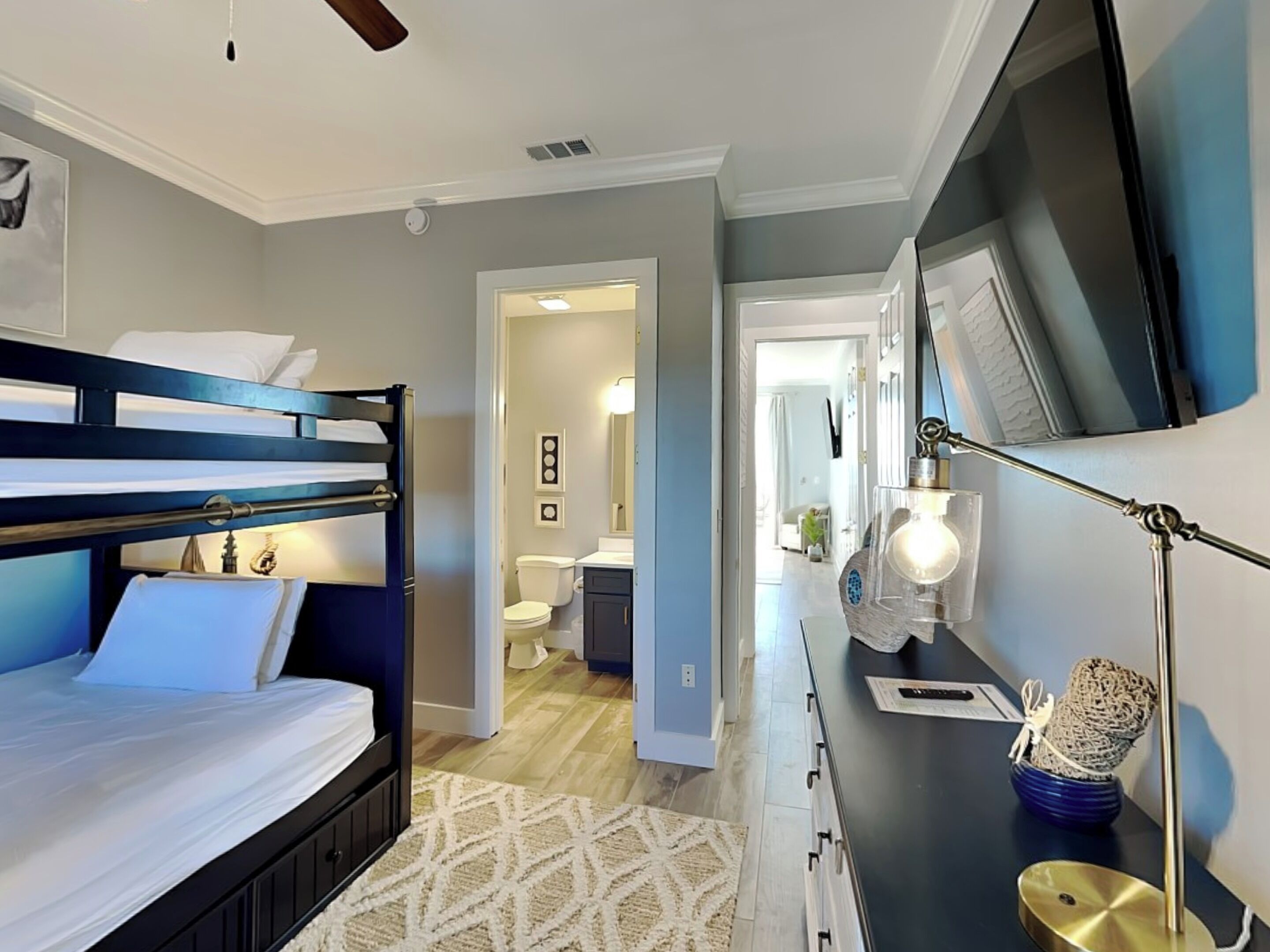 A modern hotel room with a bunk bed, a desk with a lamp, and a TV.