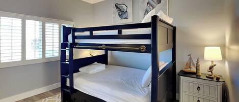 A bunk bed room with a ceiling fan, a nightstand with a lamp, and artwork on the wall.
