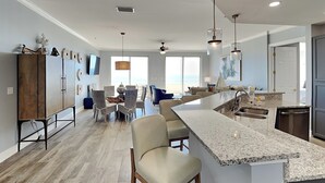 Una cuina moderna amb una illa central, zona de menjador amb cadires i vista cap a l'exterior.