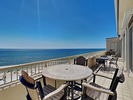 A balcony with a round table and chairs, overlooking the ocean.