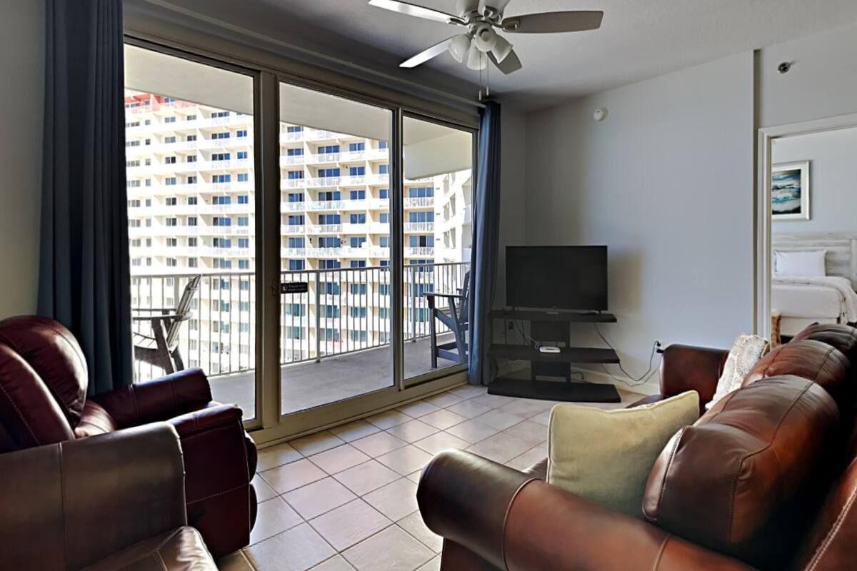 A living room with a sofa, a television, and a balcony with a view of high-rise buildings.