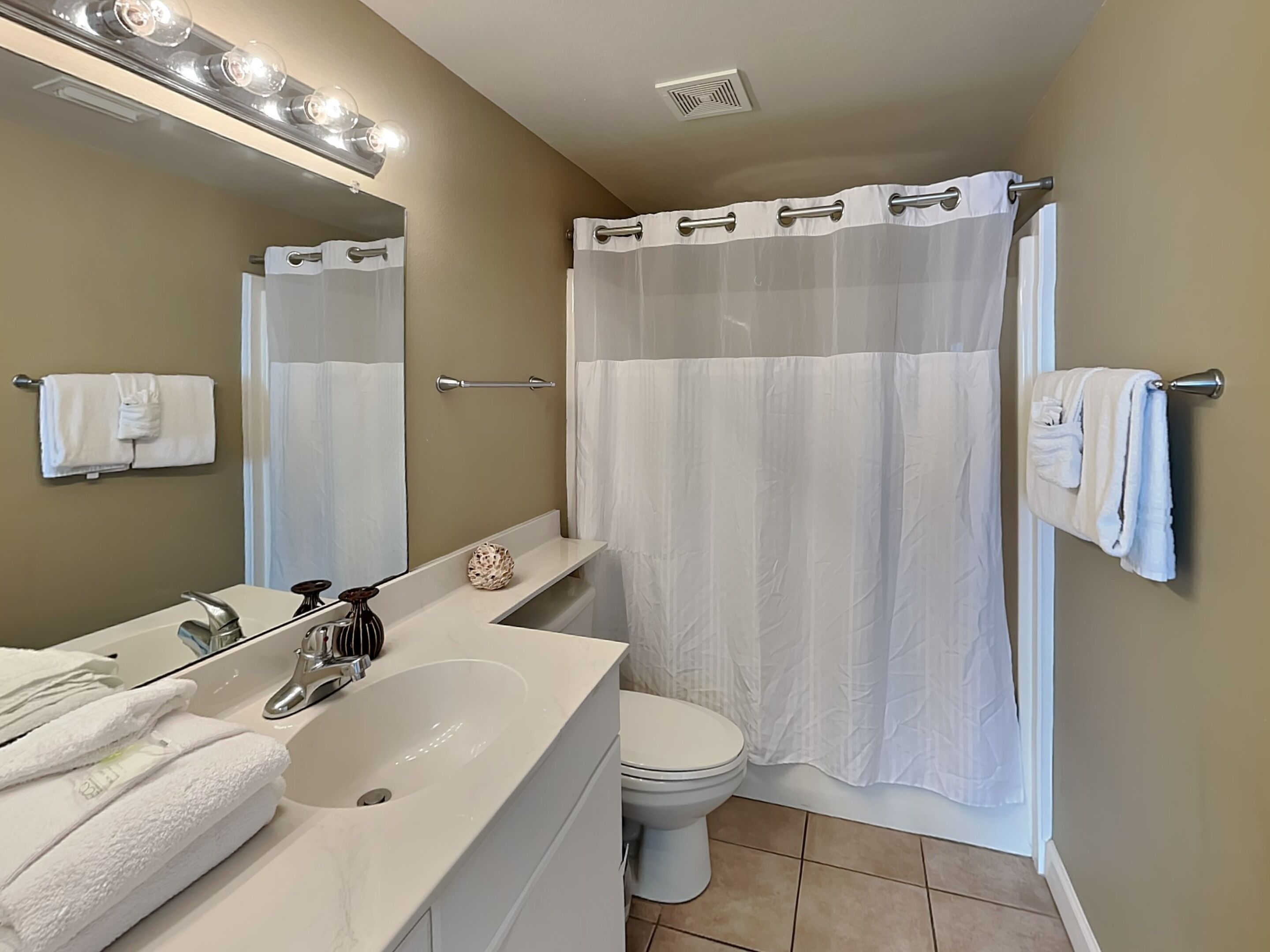 Un baño con un lavabo blanco, un inodoro, cortina de ducha y un espejo con iluminación.