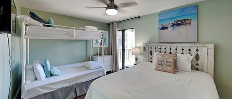 Habitación de hotel con literas, cama grande, ventilador de techo, pintura de barcos y vista al mar.