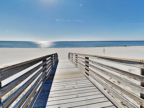 A wooden boardwalk leading to a beach with a clear sky.