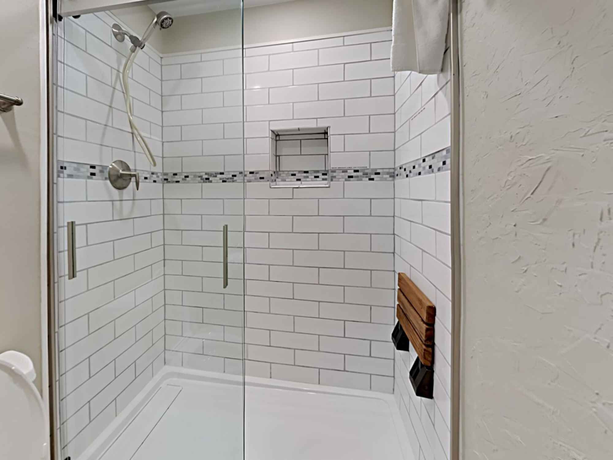 A modern bathroom with white subway tiles, a glass shower enclosure, and a wooden bench.