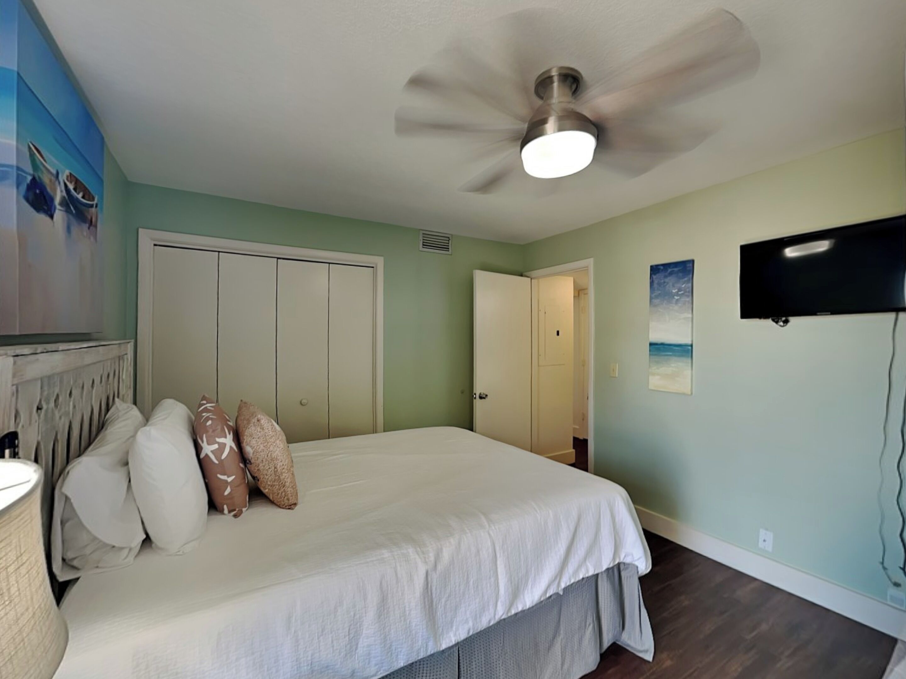 A bedroom with a bed, a ceiling fan, a TV, and a closet.