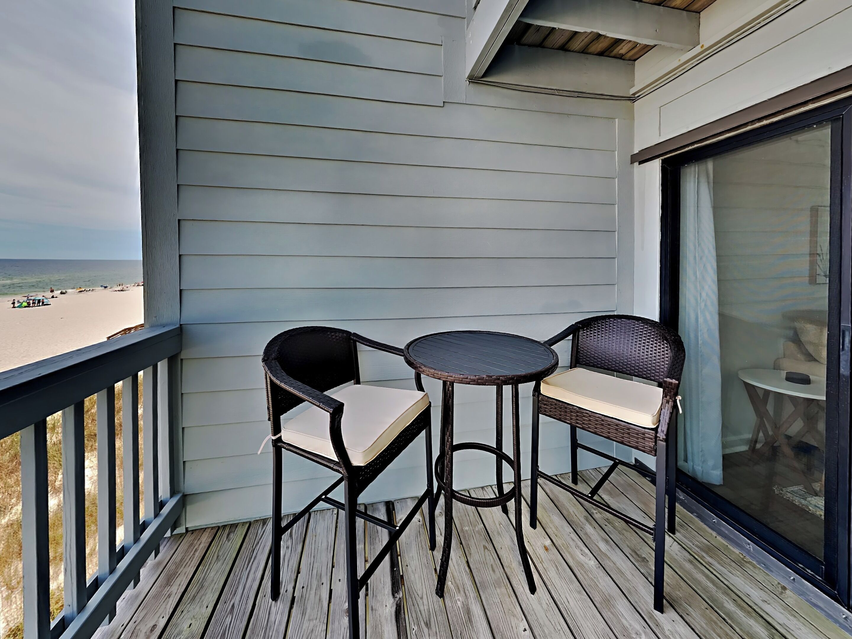 Un balcon avec deux fauteuils en osier et une petite table ronde, donnant sur une plage.