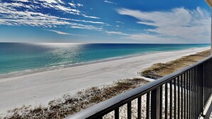 Une vue sur la plage depuis un balcon doté d’une balustrade, avec un ciel dégagé et l’océan à l’horizon.