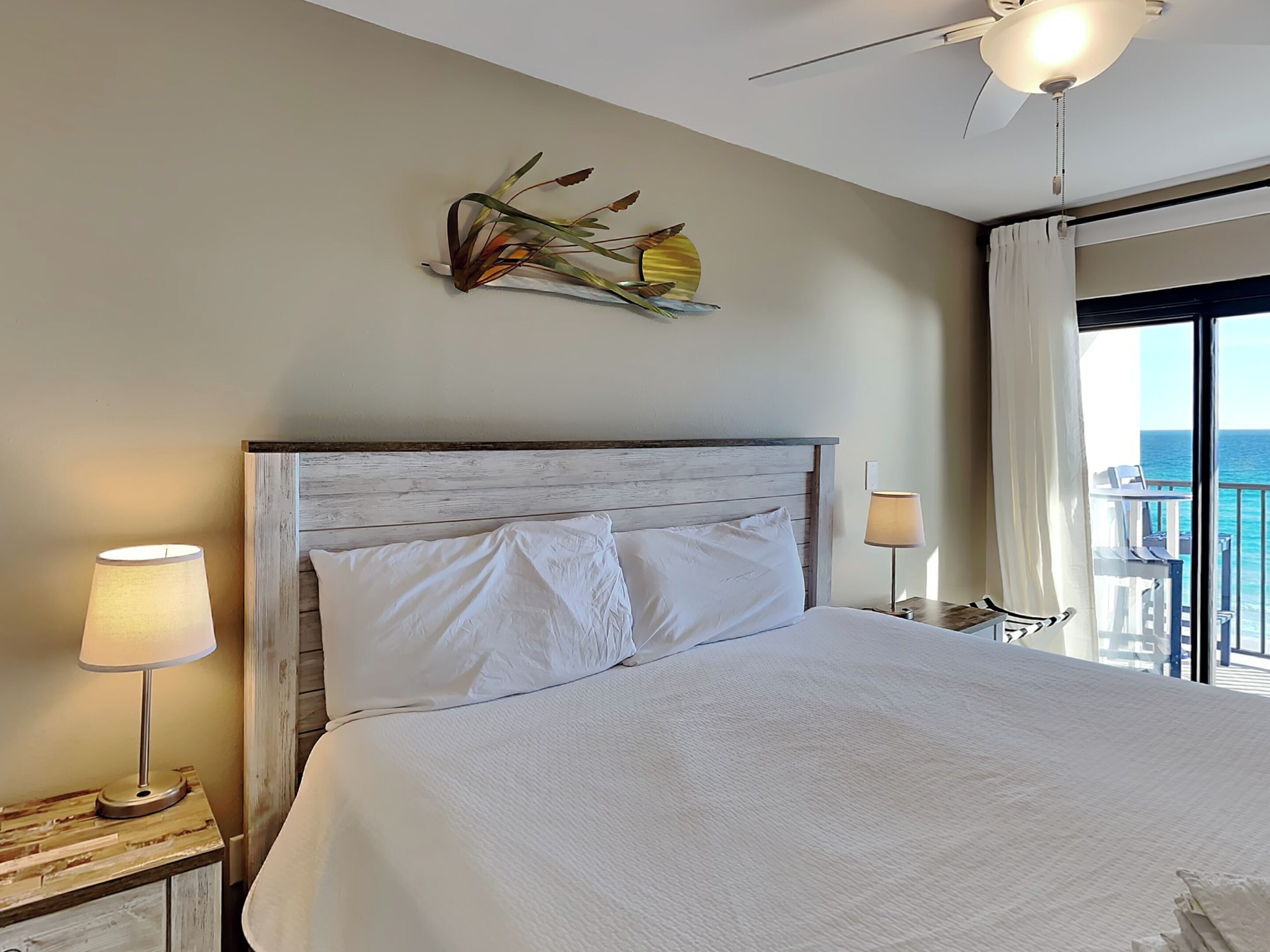 Ein Hotelzimmer mit einem großen Bett, einem Deckenventilator, einer Wanddekoration und Blick auf den Ozean.