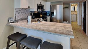 Une cuisine moderne avec des meubles blancs, un réfrigérateur en acier inoxydable, un coin café et un espace bar avec des tabourets.