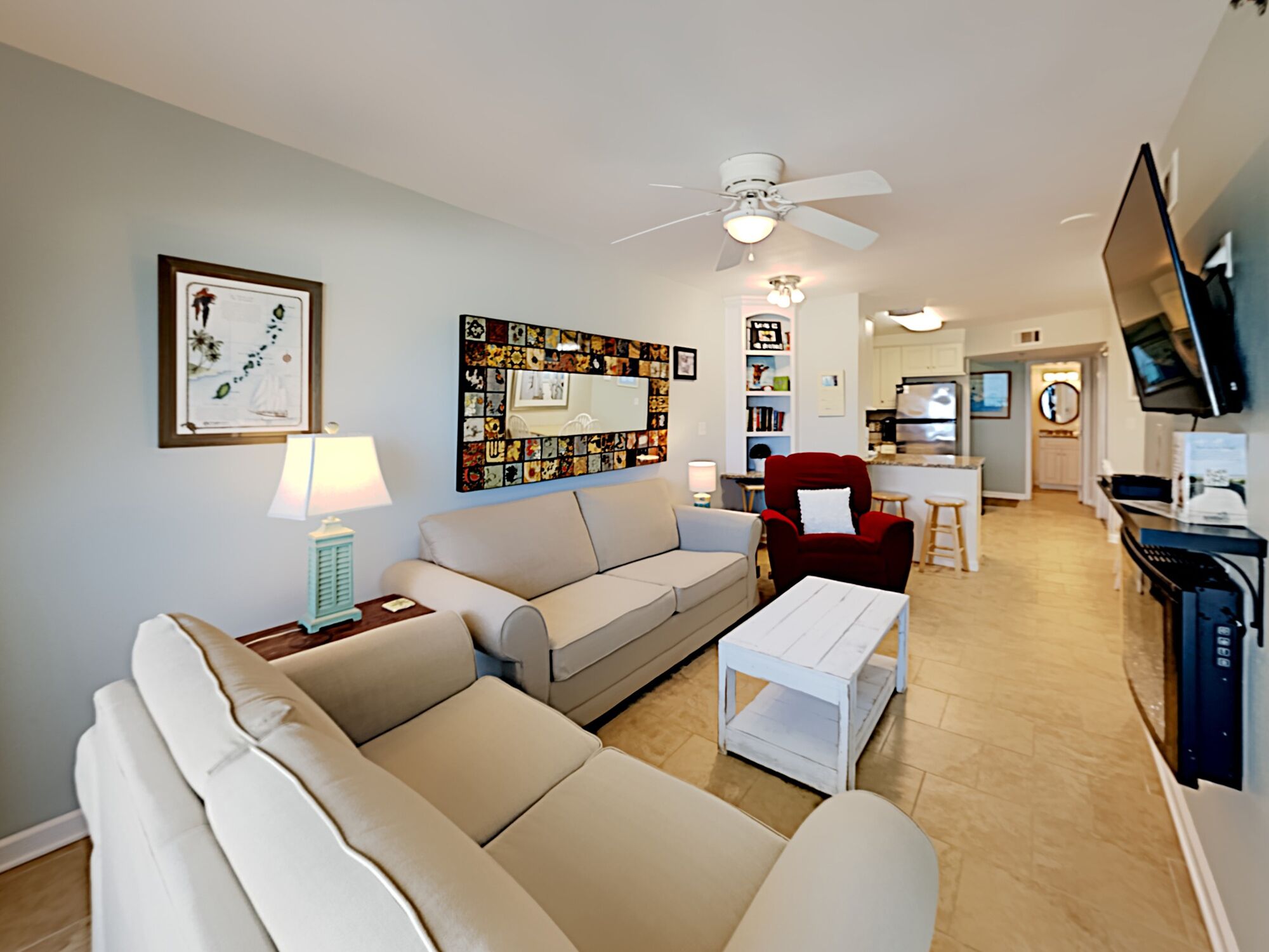 A living room with a sofa, a red armchair, a coffee table, a ceiling fan, and a TV mounted on the wall.