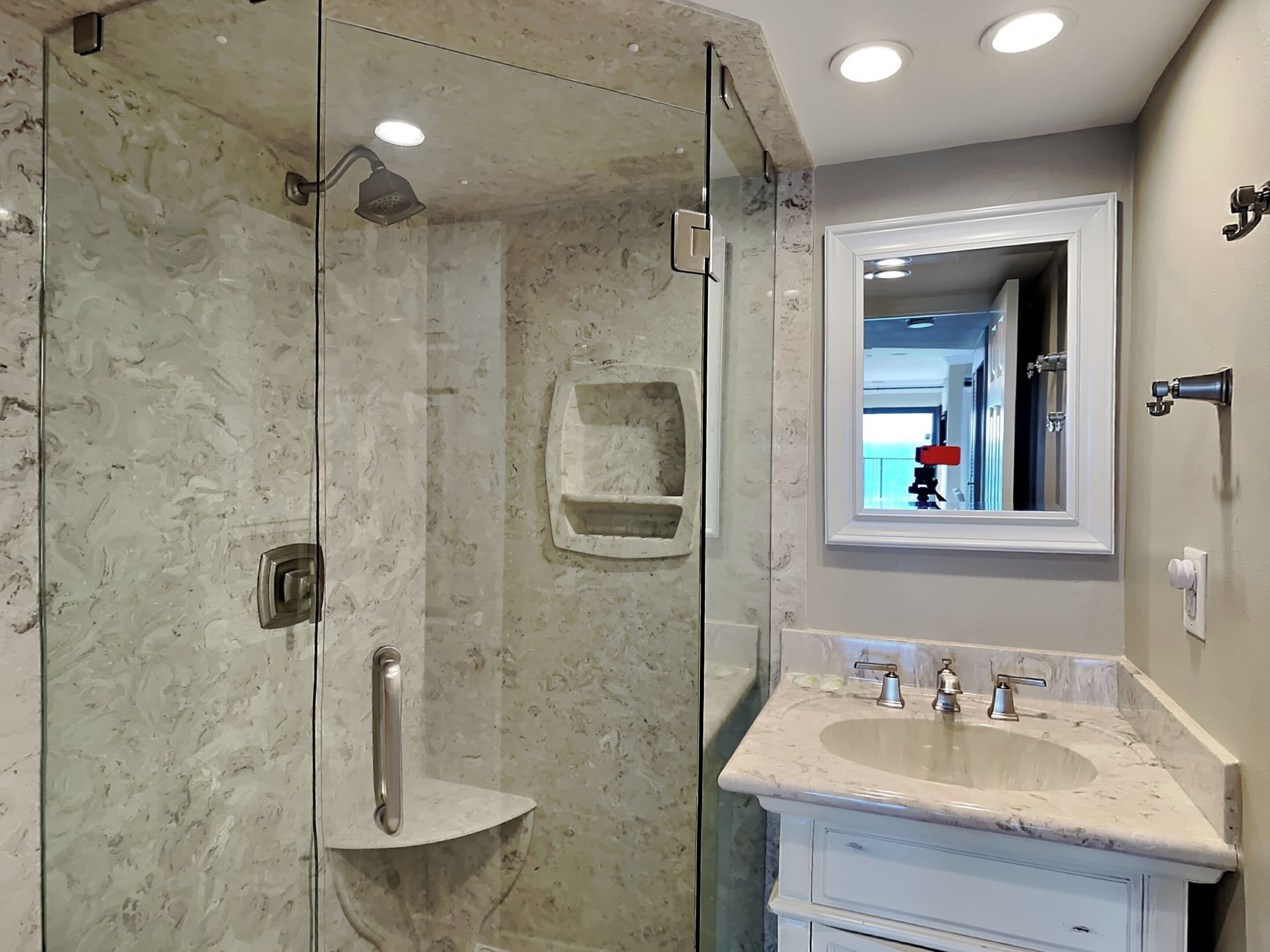 A modern bathroom with a glass-enclosed shower, a marble countertop sink, and a mirror above the sink.