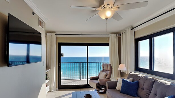 Une chambre d’hôtel avec un balcon, une télévision à écran plat, un canapé, une table basse et un ventilateur de plafond.