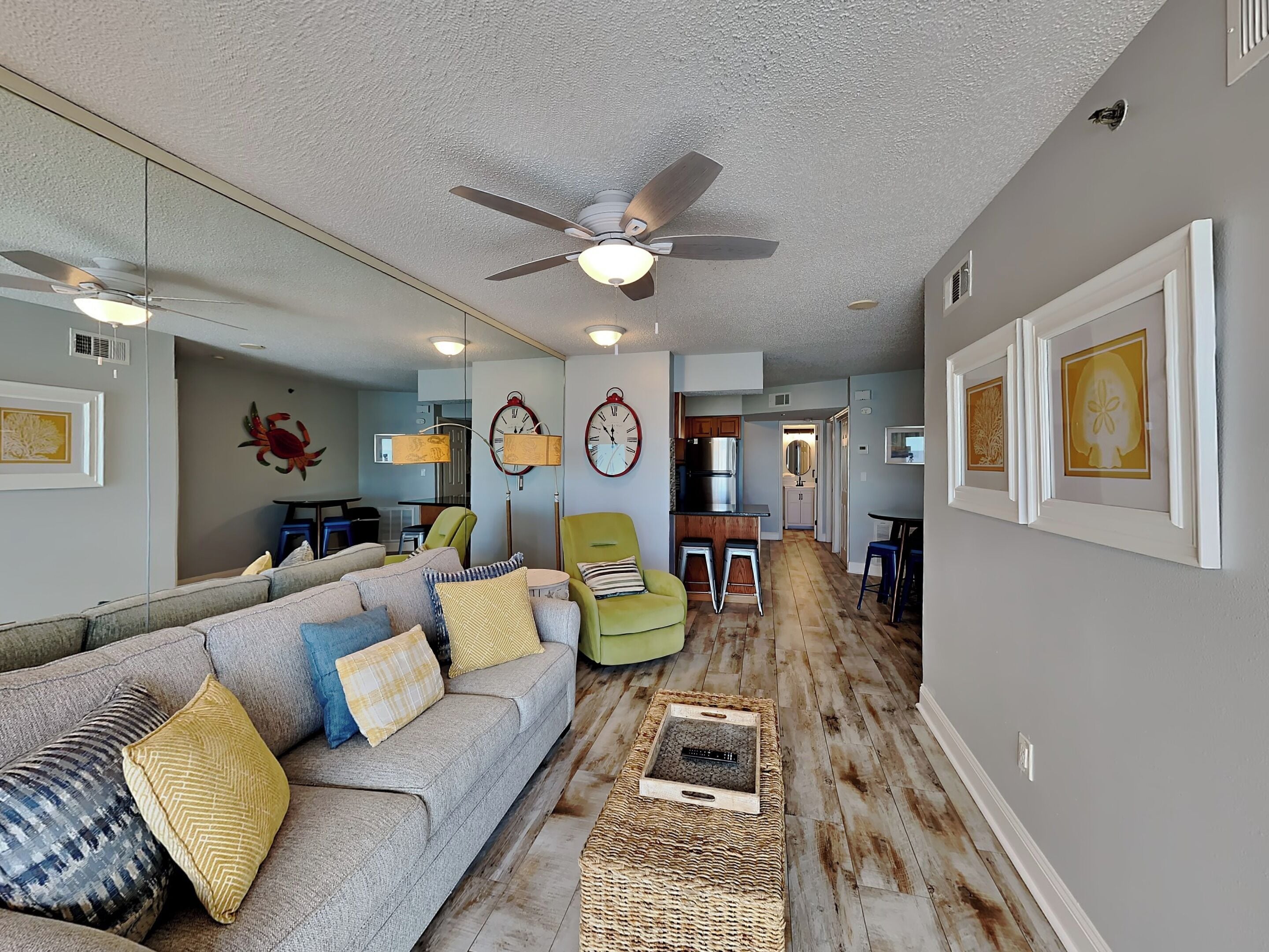 A spacious living room with a large gray sofa, a ceiling fan, and a kitchen area in the background.