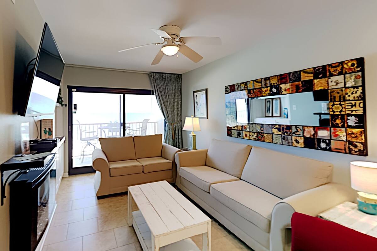 A living room with a piano, two sofas, a coffee table, a TV, and a ceiling fan.