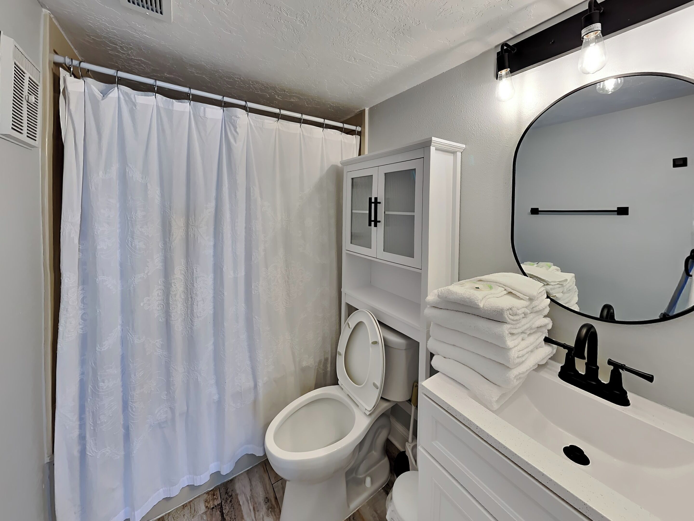 A bathroom with a toilet, a sink with a mirror, a towel rack, and a shower curtain.
