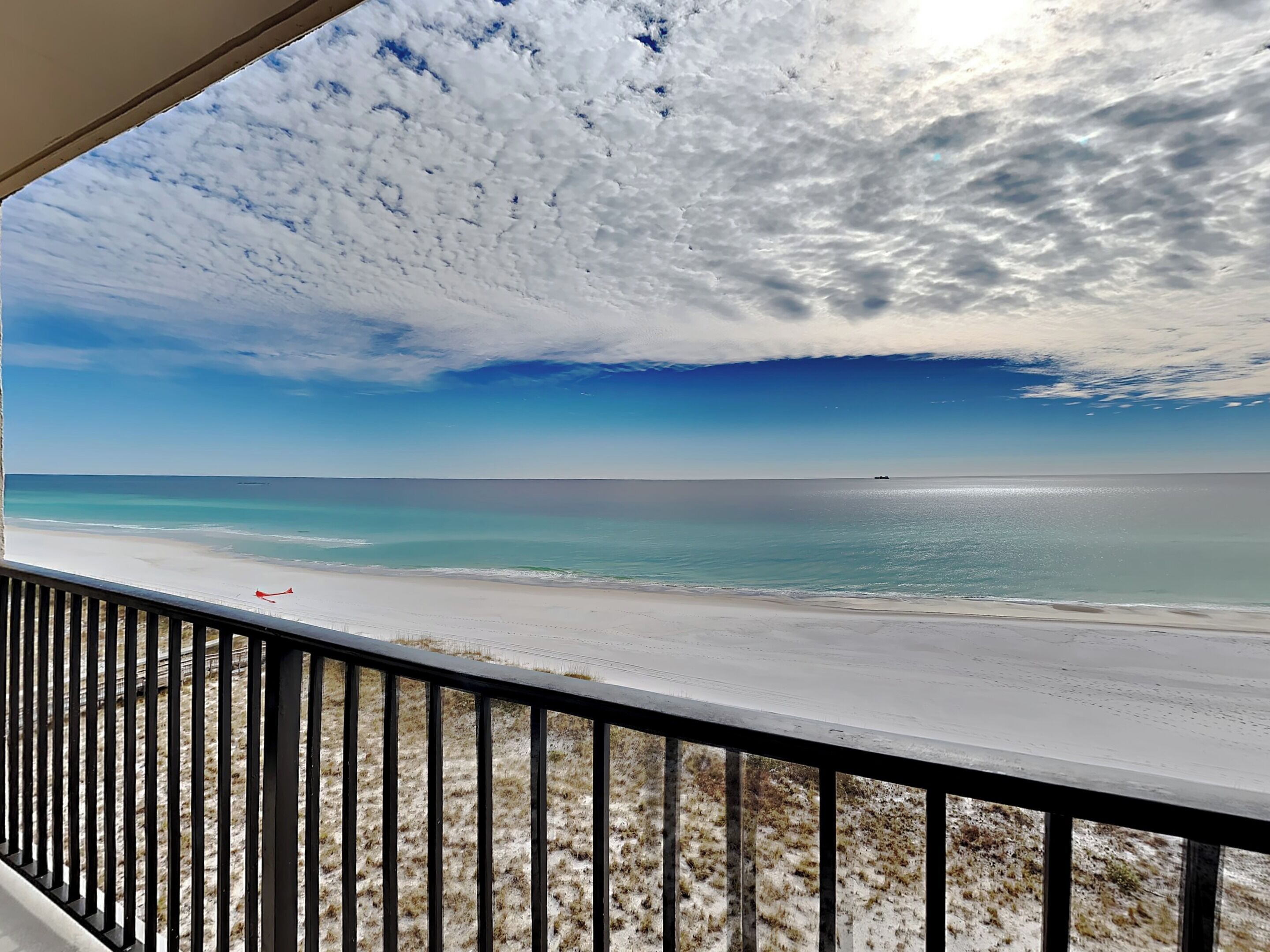 A beach view from a balcony with a railing, clear sky, and calm sea.