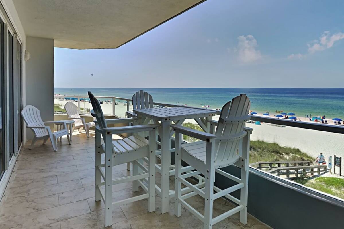 A balcony with a table and chairs overlooking a beach.