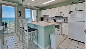 A kitchen with a view of the ocean, white cabinets, a refrigerator, and a dining area with chairs. - Silver Beach by Southern Vacation Rentals (Orange Beach)