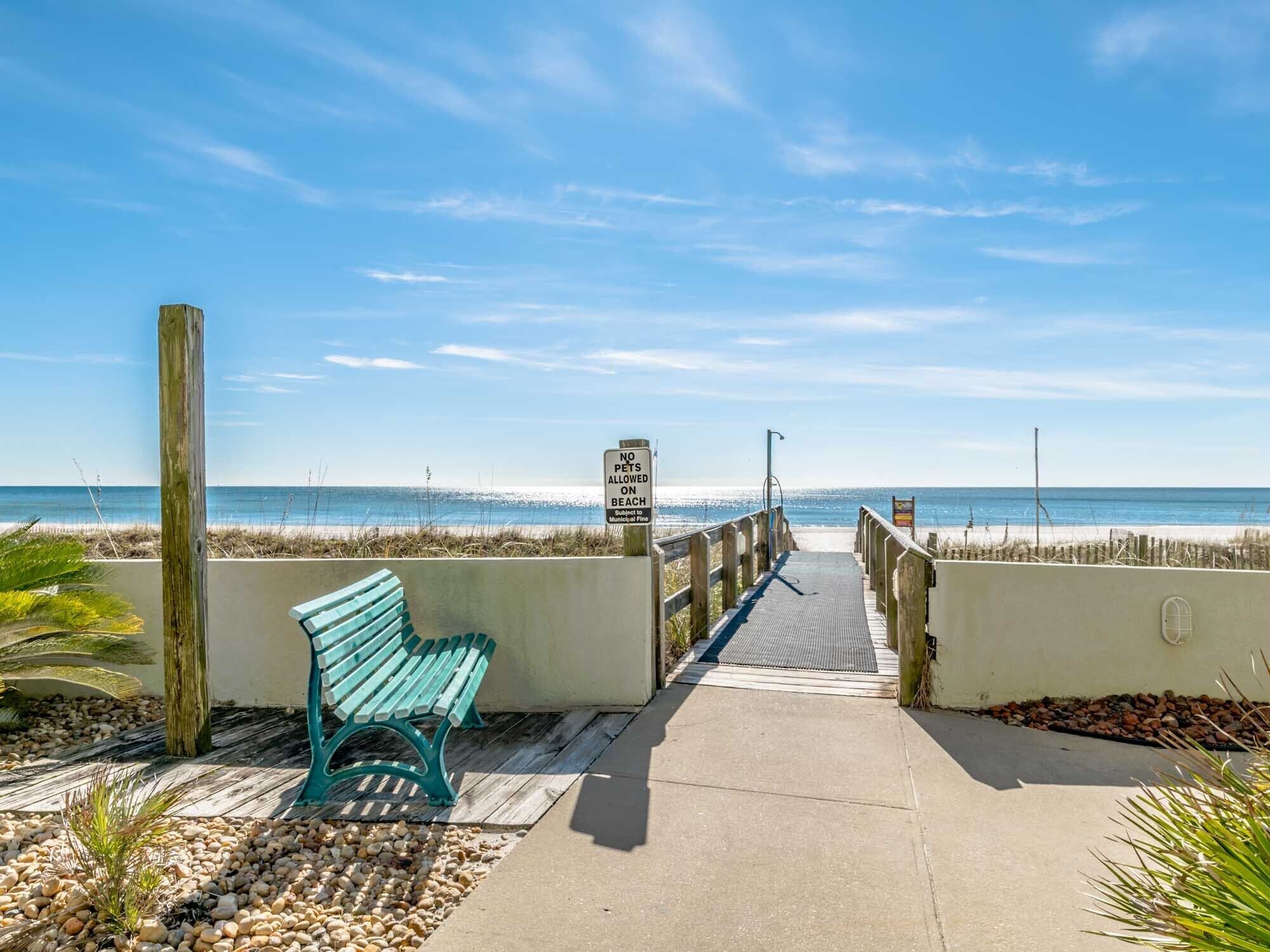 A beach walkway with a bench, a sign prohibiting pets, and a view of the ocean.