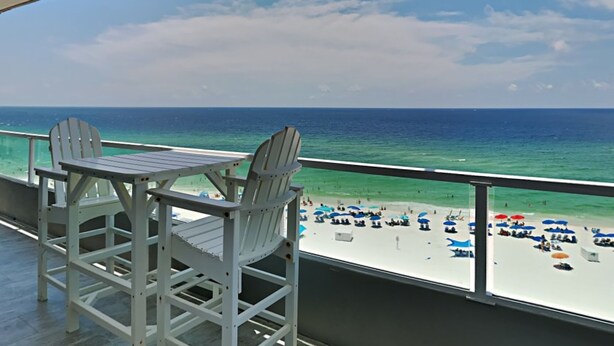 A balcony with two Adirondack chairs facing a beach with umbrellas and people. - Silver Beach by Southern Vacation Rentals (Orange Beach)