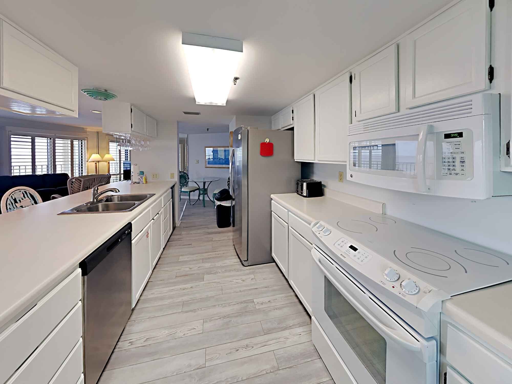 Una cocina moderna con armarios blancos, un microondas integrado, una estufa y un lavamanos.