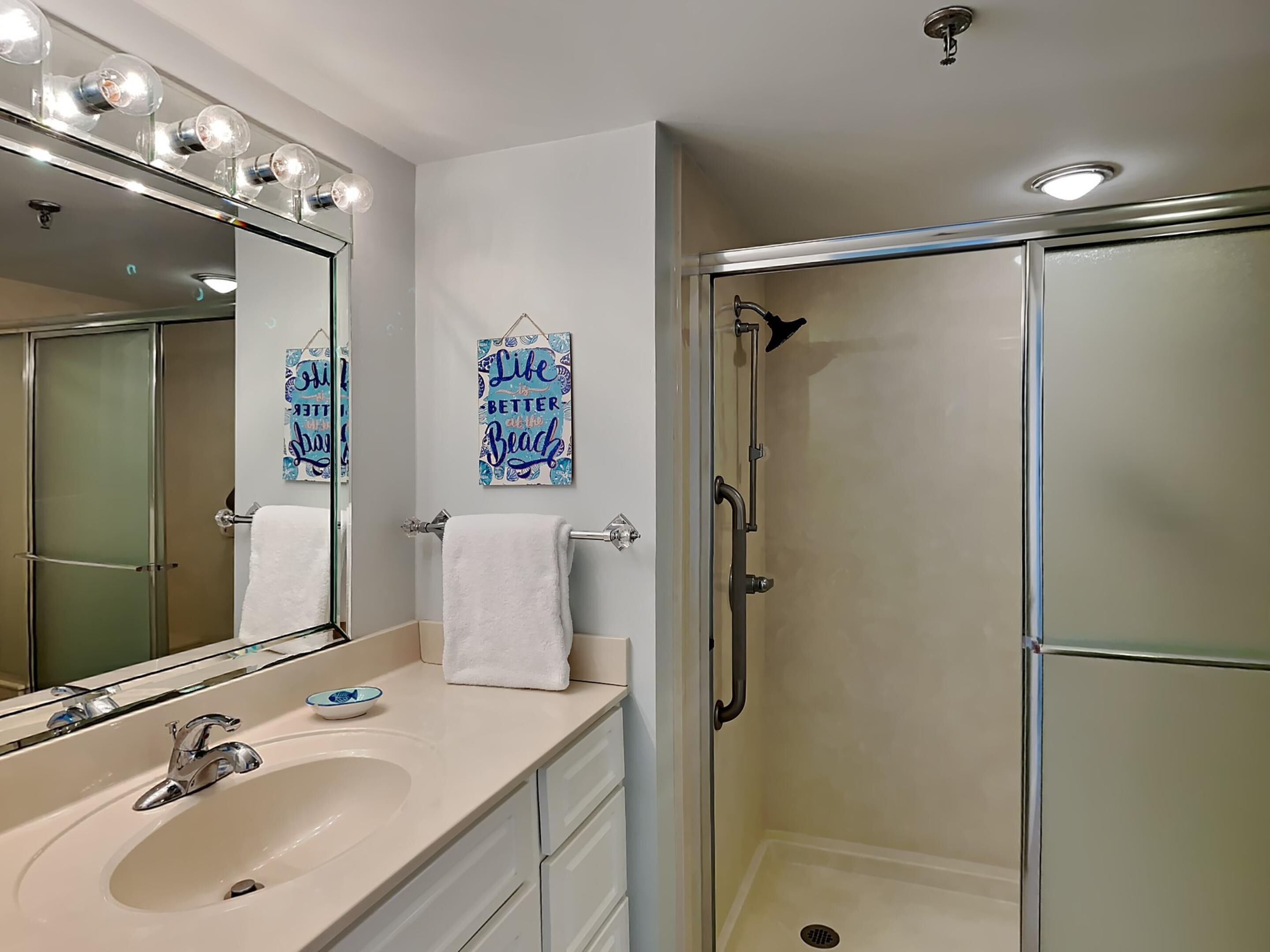 A bathroom with a large mirror, a sink, a towel rack, and a glass-enclosed shower.