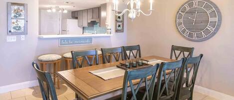 A dining area with a wooden table, six chairs, a chandelier, and a large wall clock.